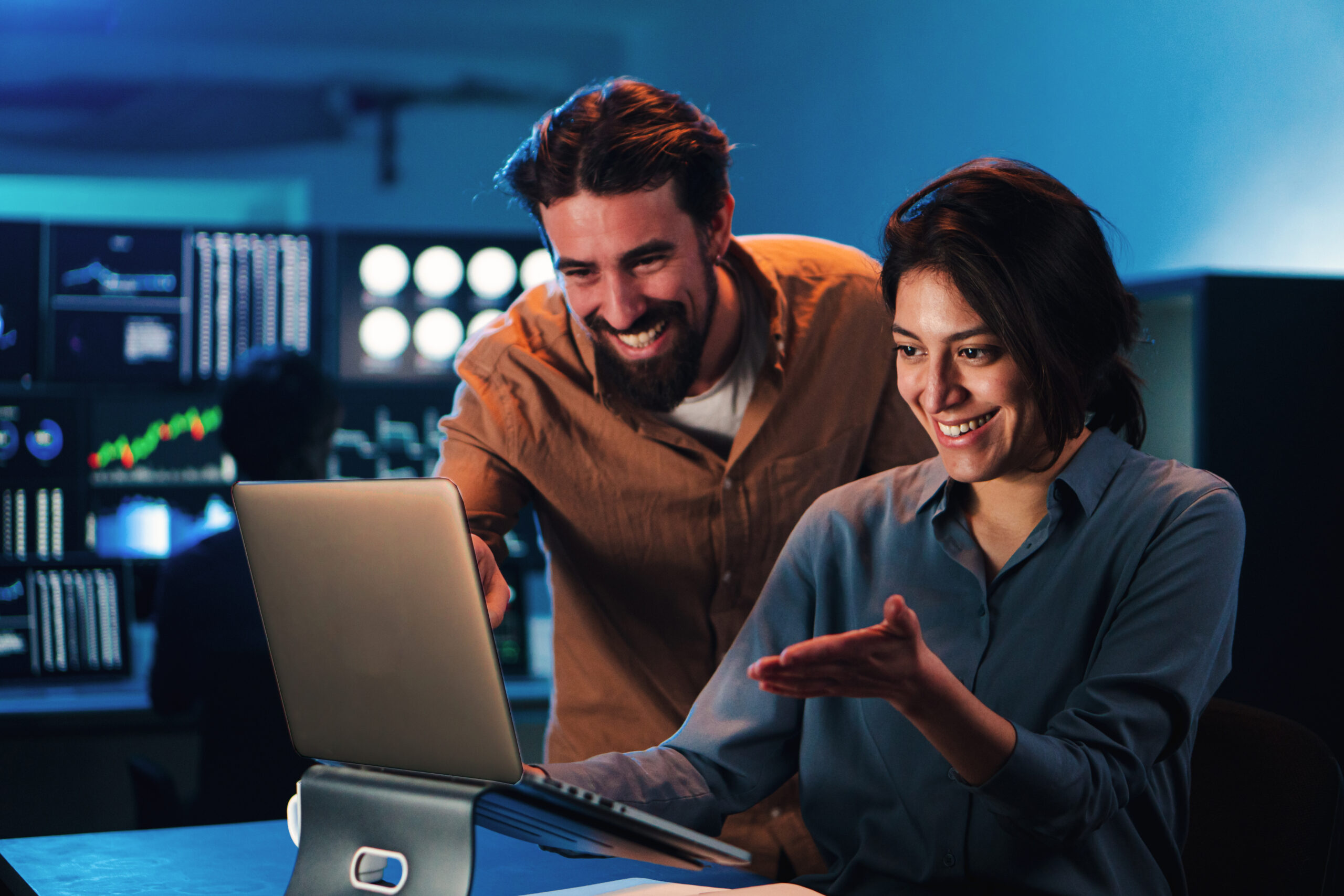 Happy business couple working on a laptop computer in the office. Young trading team people smiling watching data on pc screen. Two partners coworking on finance. High quality photo
