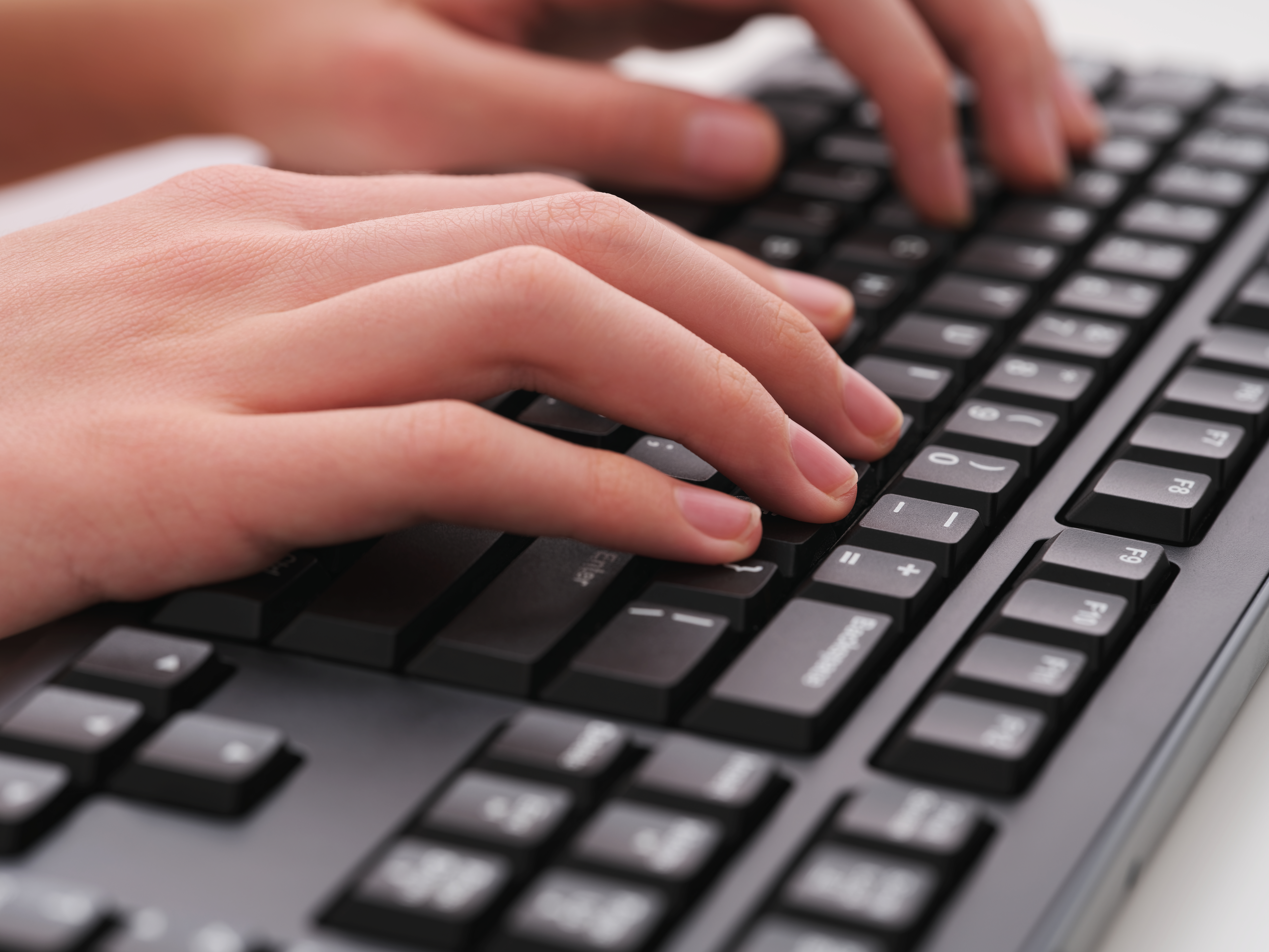 A young man typing on a black computer keyboard. Close up.